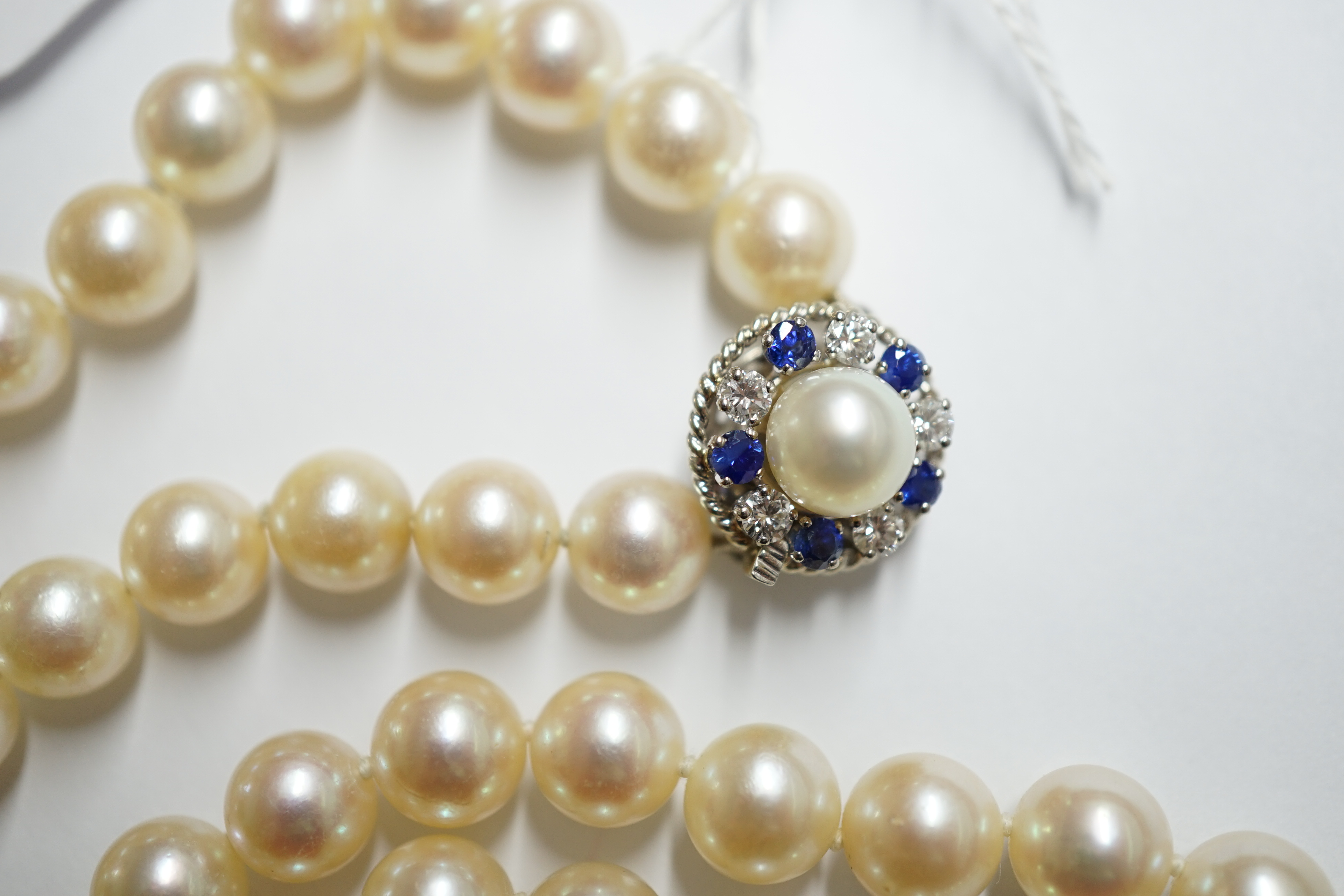 A single strand cultured pearl necklace, with French white metal (18ct mark), sapphire, diamond and cultured pearl set clasp, bearing the signature 'Cartier', 60cm. Condition - fair